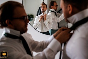 Noivo e seus padrinhos ajustando gravatas e sorrindo no espelho na casa do noivo em Noord Holland, capturado pelo fotógrafo de casamento.